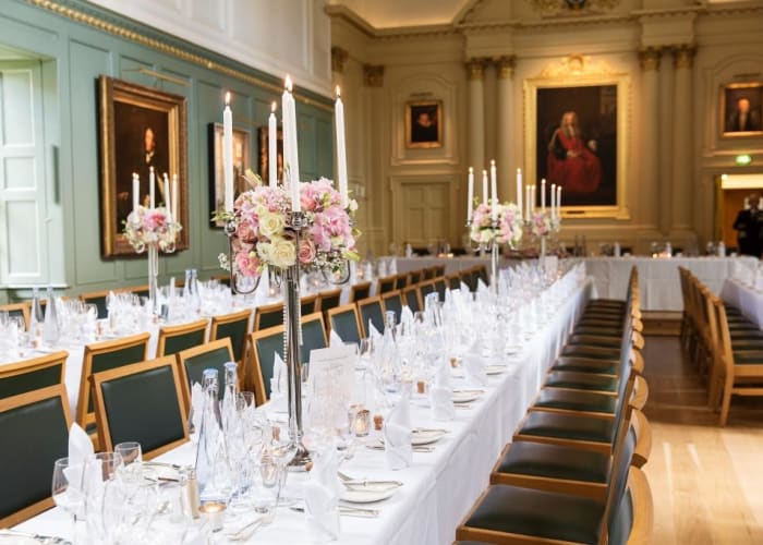 The dining hall at Trinity Hall set for private dining, fresh flowers and large candlesticks complete the table dÃ©cor.