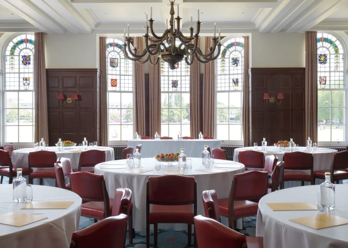 The grand Crick room, set with round tables and chairs for a day meeting, with a chandelier and stained glass windows.