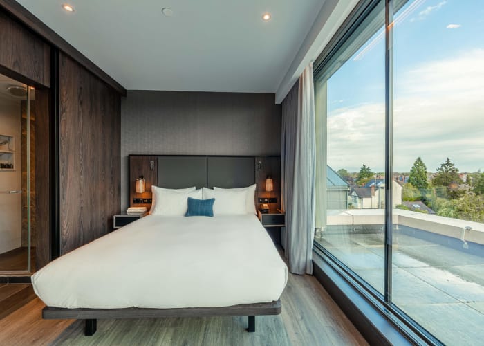 The Deluxe Studios at The Fellows House Cambridge, Curio Collection by Hilton. With floor to ceiling windows, the rooms feature a walk in shower and large spacious and luxurious bed.