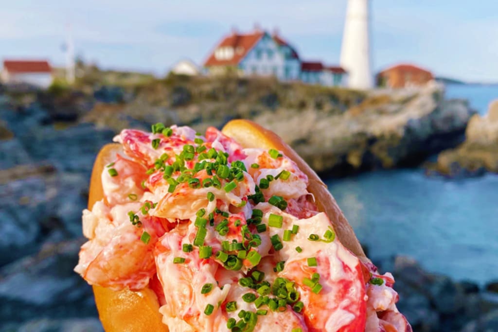 Lobster Roll in front of Portland Head Light. Photo Credit: Bite Into Maine
