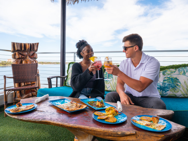 Two people toasting and dining outdoors at Pier Teaki.