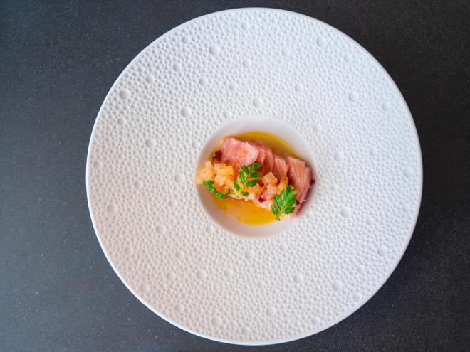 a white plate with a wide dimpled rim, with delicate raw fish and garnish in the middle