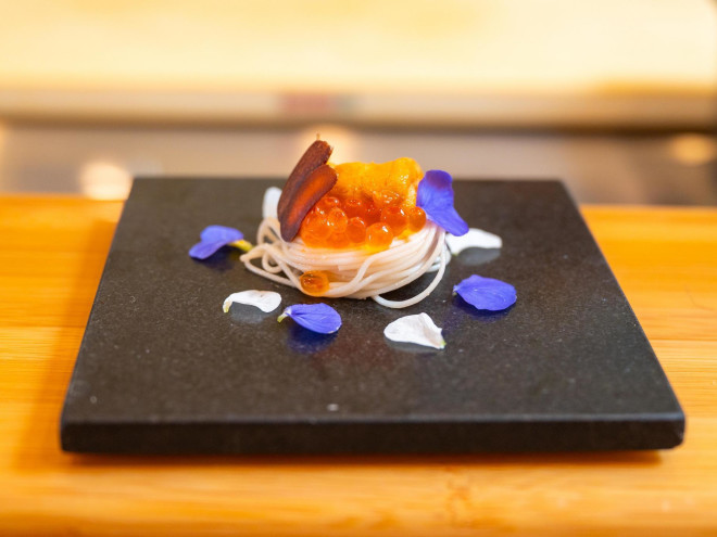 a beautifully plated sashimi decorated with purple flowers on a black slate plate
