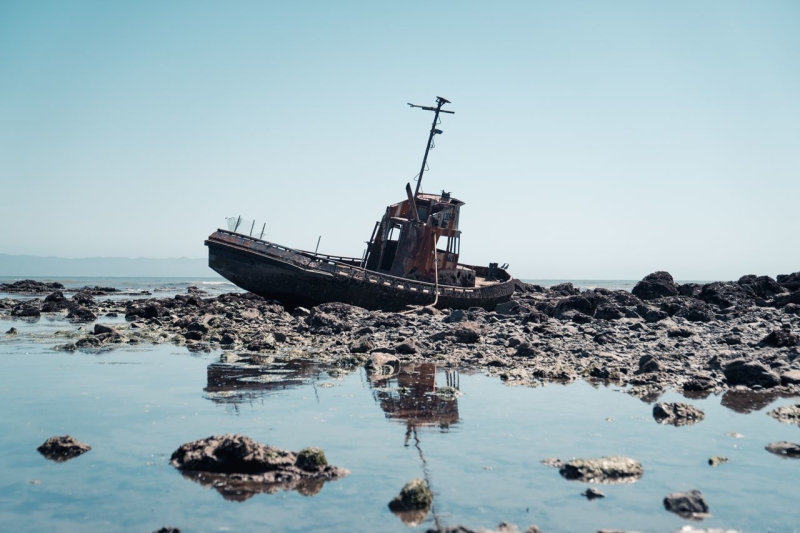 Shipwrecked boat on rocks with shallow water in the foreground