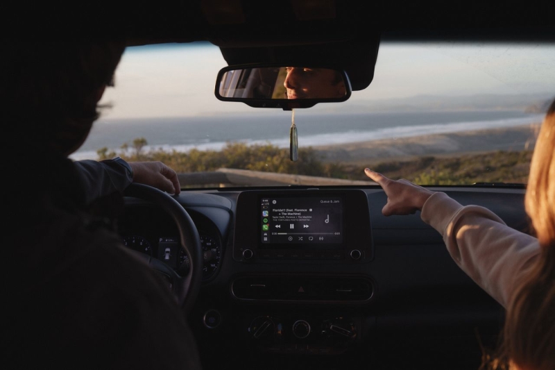 View through a car windshield with two people inside pointing and looking at coastal view