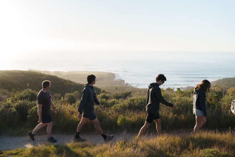 Group of hikers walks a coastal trail at sunset with ocean views and grassy dunes in Montana de Oro.