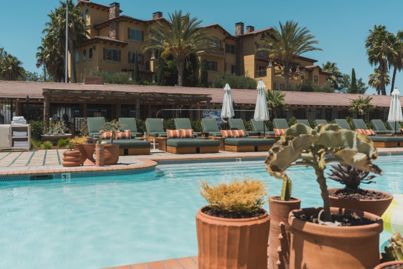 Pool in the sun with pool chairs and building in background