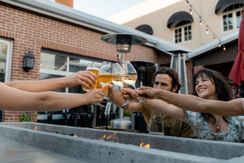 Group cheersing wine above a fire table outdoors in downtown Paso Robles with brick building and string lights in background