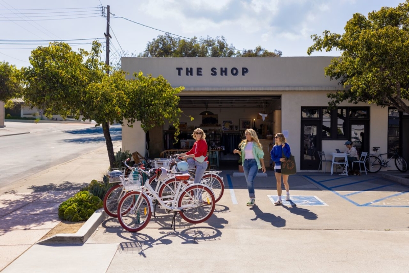 Three women walking to bikes parked outside of a building called "The Shop"