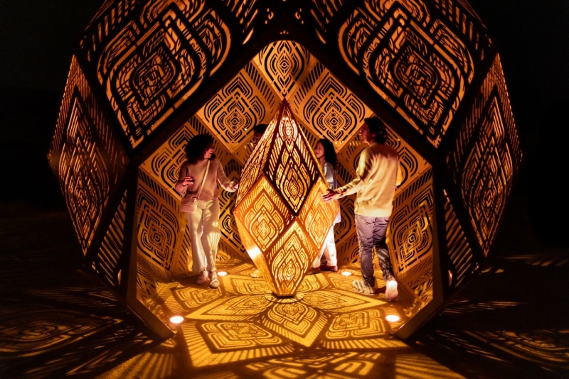 People inside sculpture walking around with floor lights casting shadows
