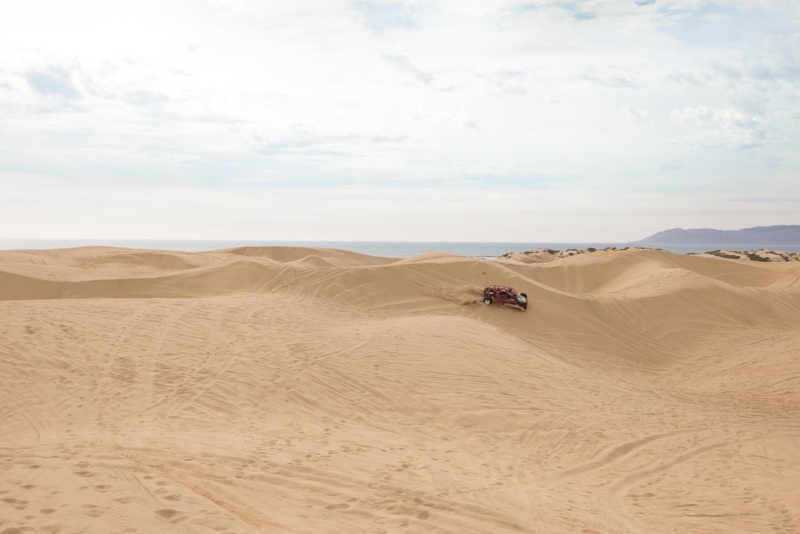 Car driving on large sand dunes with ocean in background