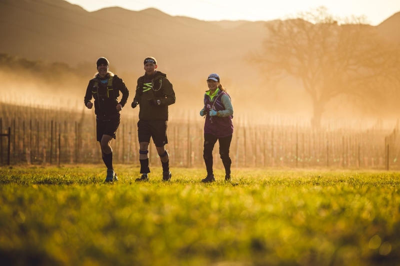 Two men and one woman running through field during golden hour at the Spartan Race