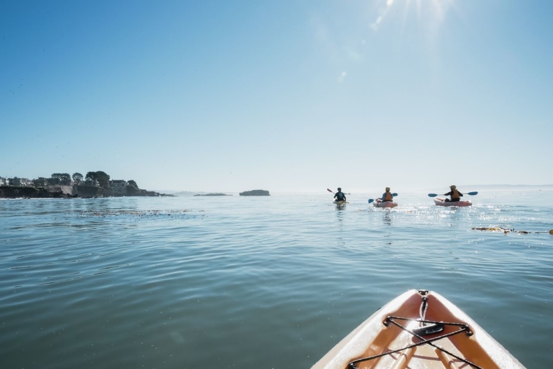 View on flat water and horizon of three kayakers with the tip of a kayak seen from photographer
