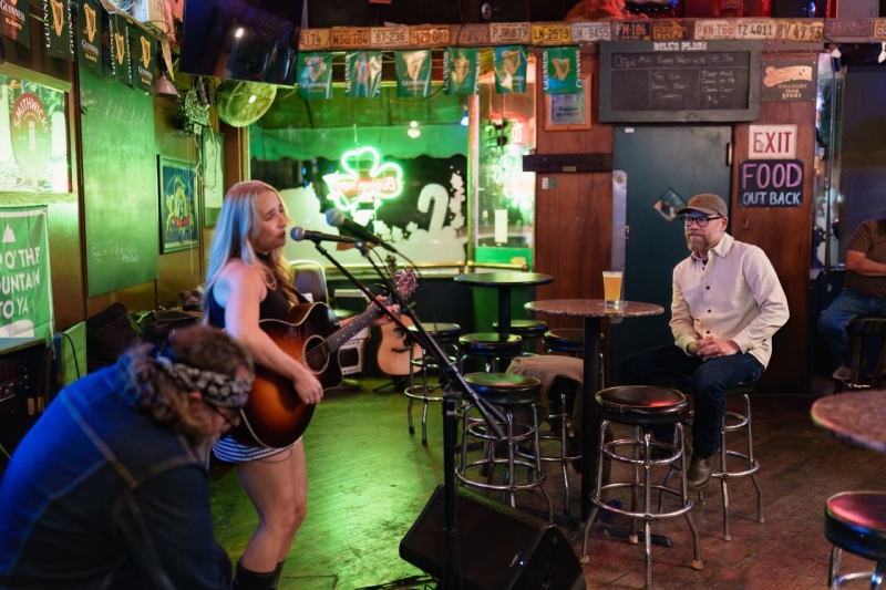 Musicians playing guitar and singing at bar with person watching from a table with a beer
