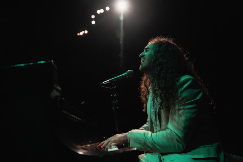 Nico Larson of Próxima Parada playing piano and singing with spotlight.