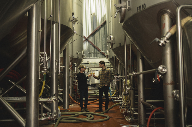 Two people cheersing beer between beer tanks