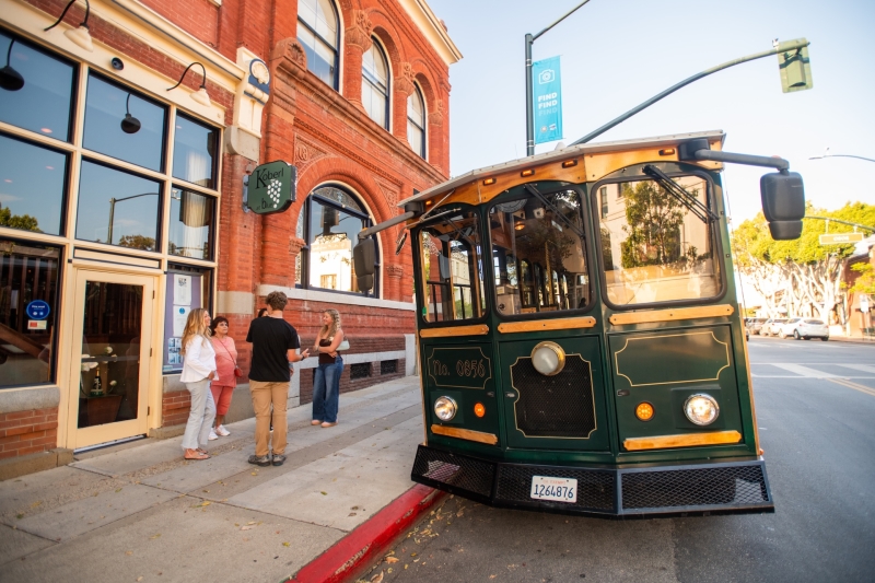 Exterior view of Old SLO Trolley, Four riders standing outside on Downtown San Luis Obispo street
