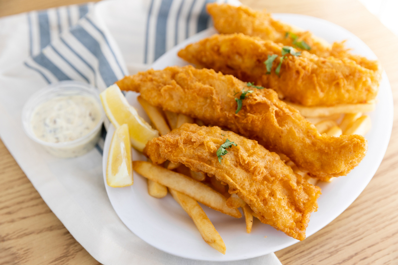 Image of breaded fish over french fries with lemon and tarter sauce on a plate