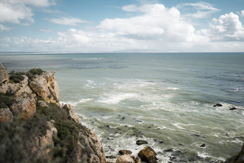 View from rocky cliffside of ocean horizon with blue sky and clouds