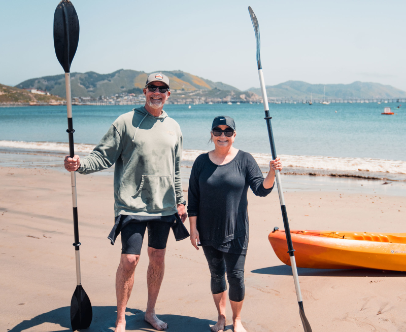 Couple holding kayak oars standing on the beach in Avila Beach