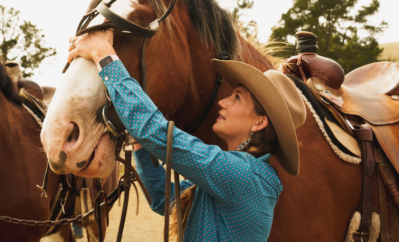 Women with cowboy hat getting horse ready to ride