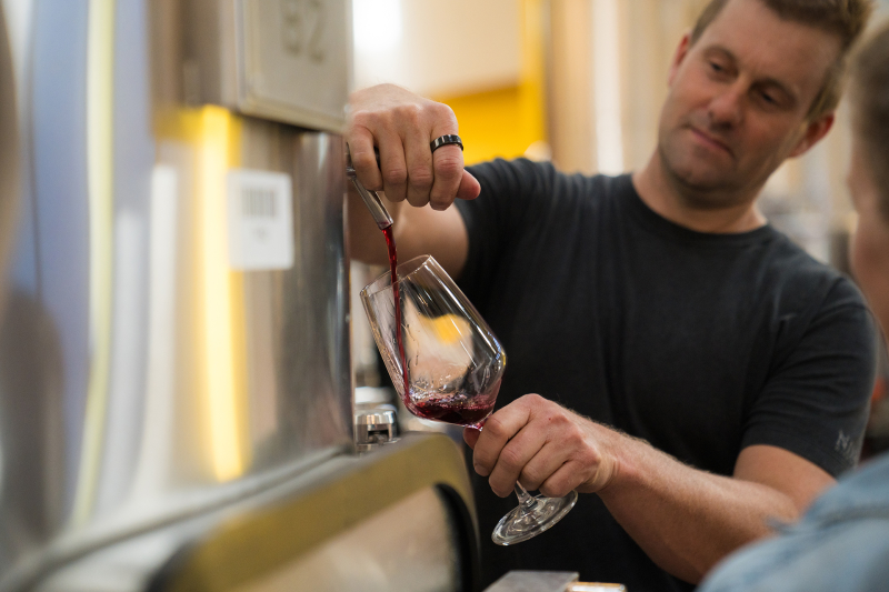 Man pouring red wine into a glass from a barrel