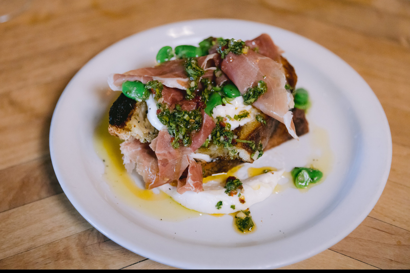 Colorful bread, meat, and greens dish on white plate