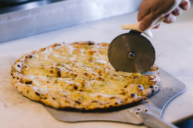 Close up of a cheese pizza on a pizza sheet getting sliced by a pizza cutter