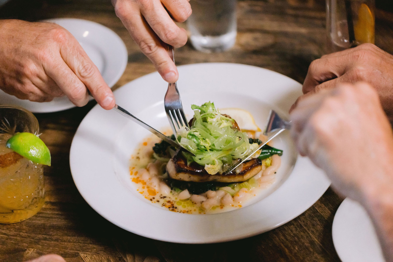 Hands of two people cutting into a fish dish