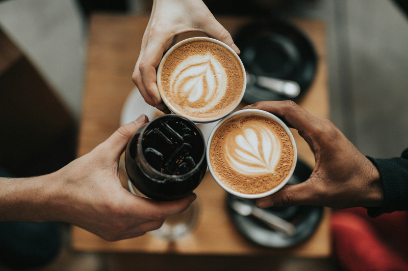 Three coffees raised together over a table