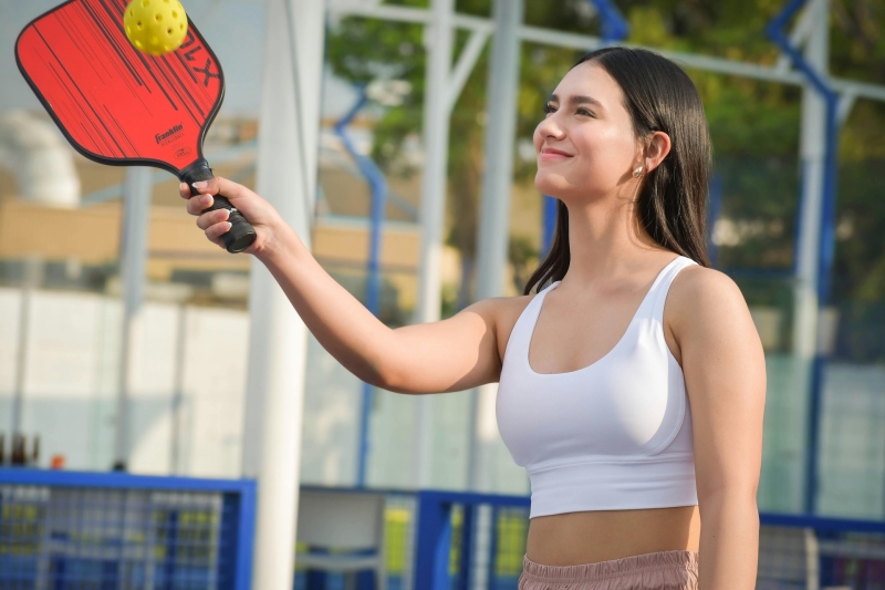 Woman holding a red pickleball racket in her hand, returning a ball on an outdoor court