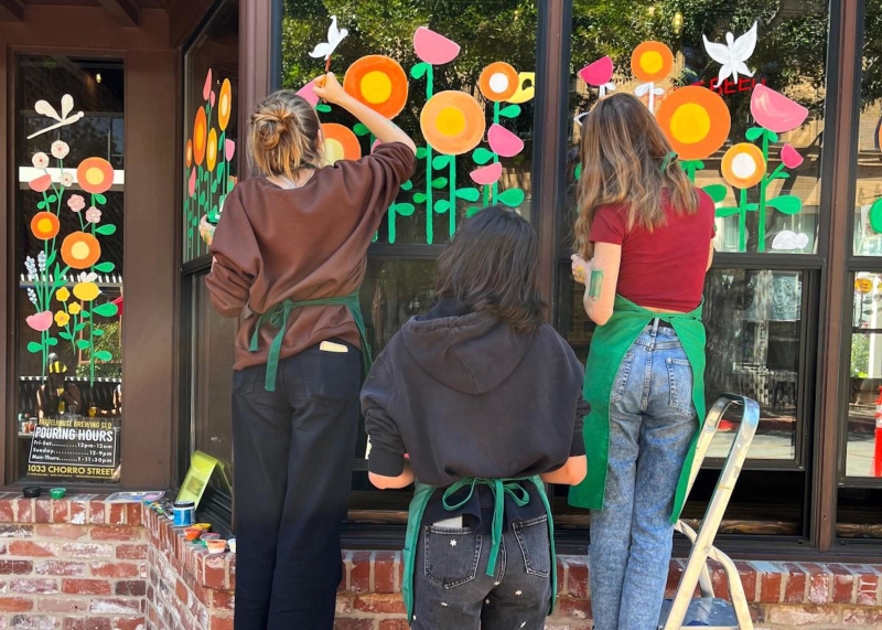 three artists painting a flower mural on a Downtown SLO window