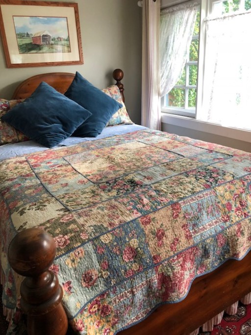 Bedroom with queen bed, lace curtains, and drapes.