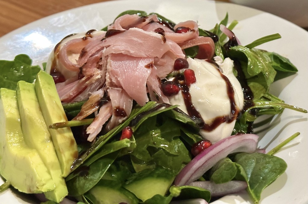 Pomegranate Winter Greens with Prosciutto and Burrata - Arugula, spinach, avocado, cucumber and onion with prosciutto, burrata cheese, pomegranate and balsamic vinaigrette  GF  Veggie and Plant-Based option