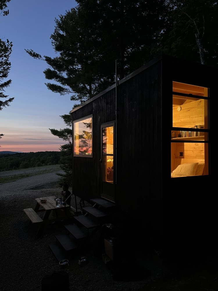 A Forest Cabin in the gloaming. These cabins feature black wood cladding to minimize their visual impact and blend them into the shadows of the surrounding wooded landscape.