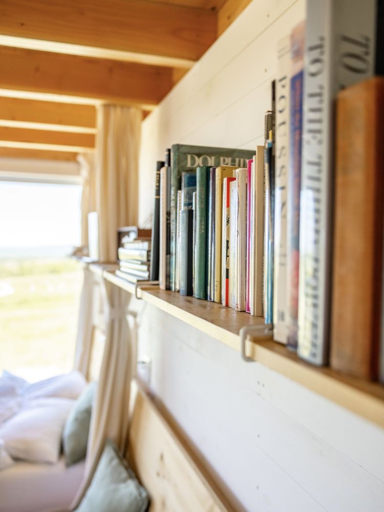 Cozy reading nook and built-in bookshelf detail inside a Field Cabin, showcasing local literature and warm wood finishes.
