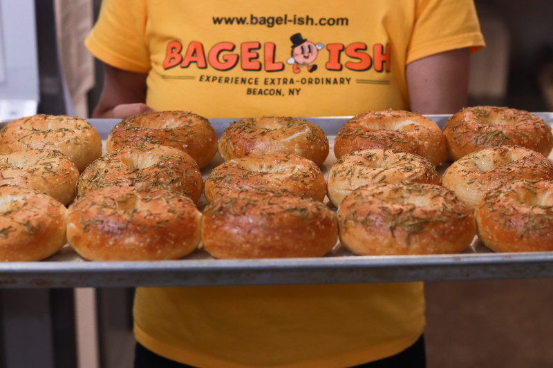                         Tray of freshly made bagels held by owner
                        