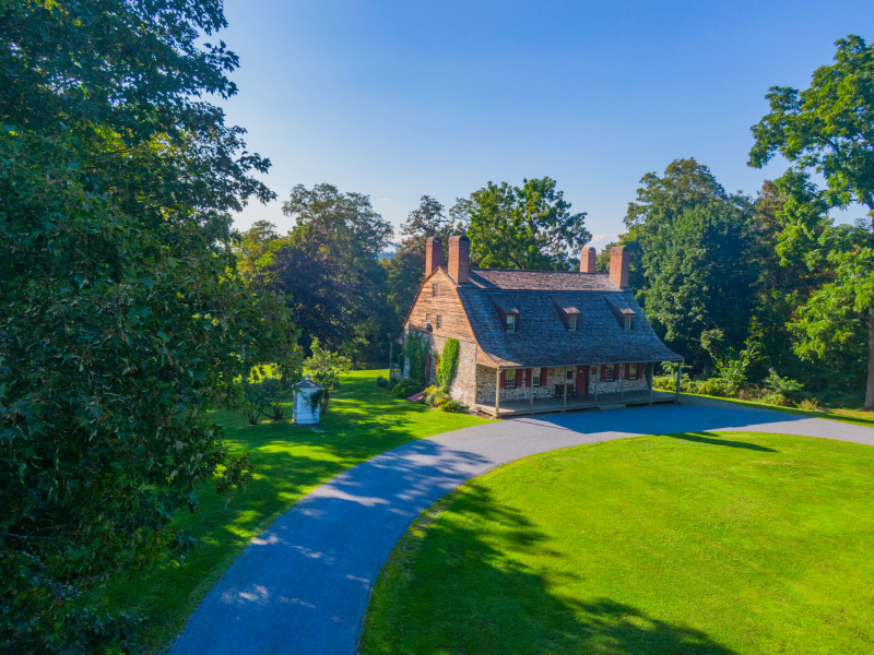                         1730 stone and wood Dutch historic home surrounded by green trees under a blue sky.
                        