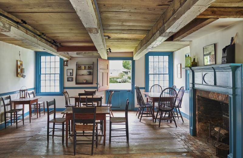                         Low wood ceiling room. Tables and chairs set-up and a light blue fireplace on the right side.
                        