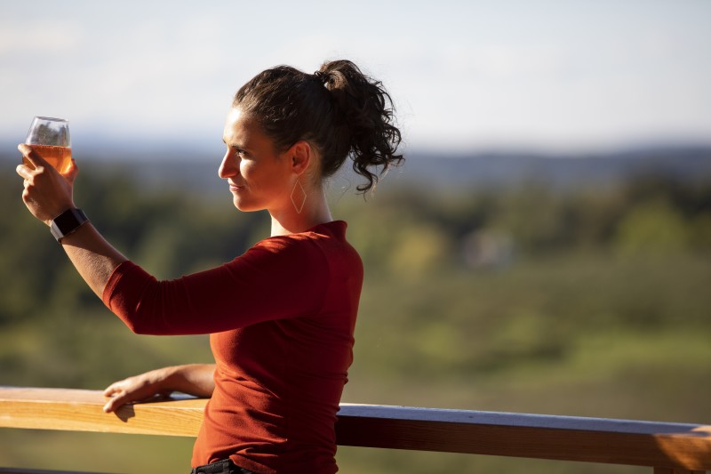                         Woman on a porch lifting and looking at cider in a glass
                        