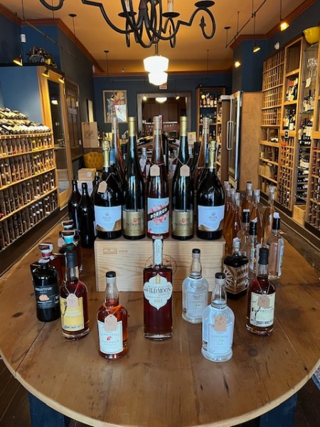                         A wooden table displays various bottles of wine and spirits in the center of the shop at Millerton Wine & Spirits.
                        