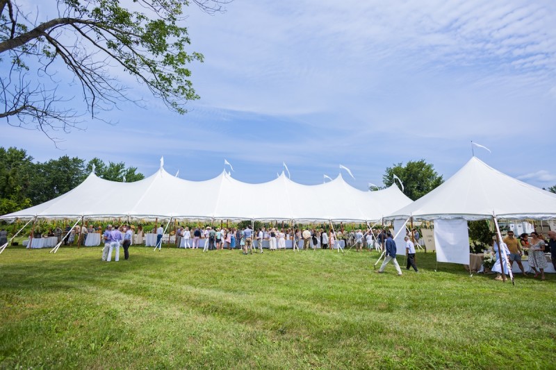                         Large outdoor event tent with attendees under s blue sky
                        