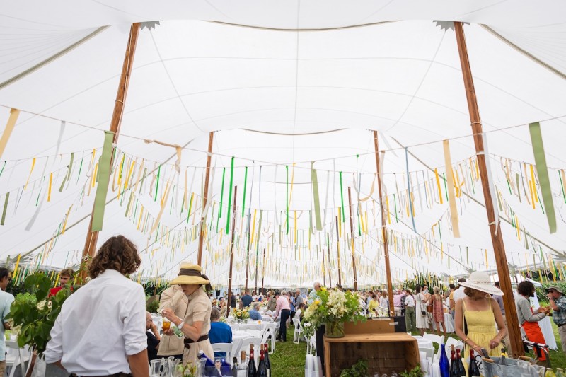                         View of the inside of event tent decorated with ribbons and active with attendees socializing
                        