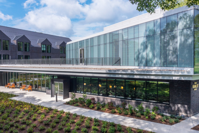                         An exterior photo of the Heartwood at Vassar, with lush green plants growing alongside its gray sidewalks and a blue sky overhead.
                        