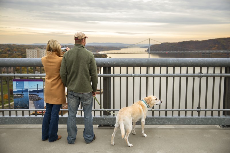                         Couple and dog looking out at the Mid-Hudson Bridge from the Walkway Over the Hudson State Historic Park in Poughkeepsie, NY.
                        
