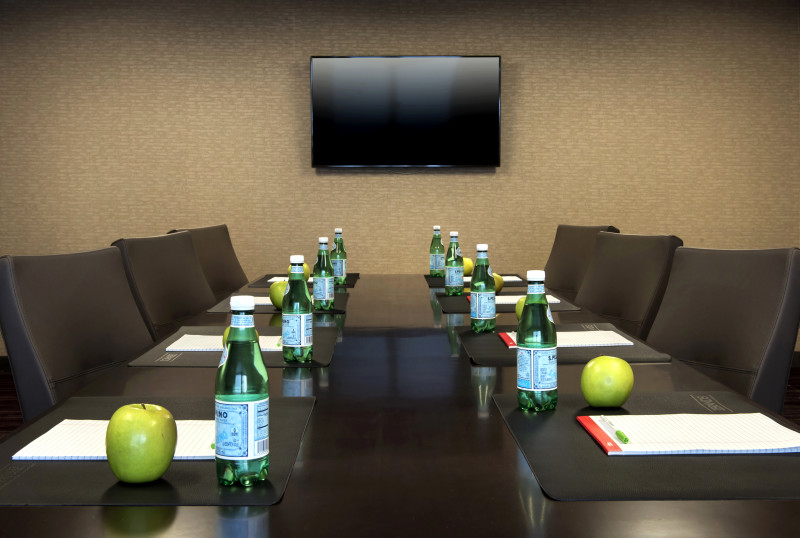                         A long conference table and chairs at the Courtyard by Marriott Poughkeepsie with note pads, water bottles and green apples neatly set up at every place setting.
                        