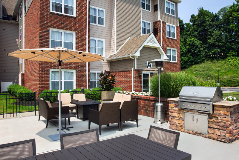                         The outdoor Patio at the Residence Inn by Marriott Poughkeepsie with chairs, tables, umbrellas and a grill.
                        