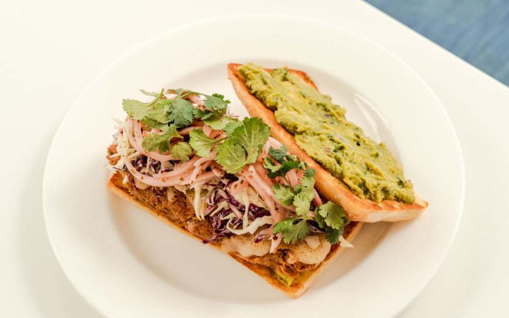 The Chicken Tinga Torta features tender shredded chicken nestled between soft bread, complemented by creamy avocado for a perfect bite.