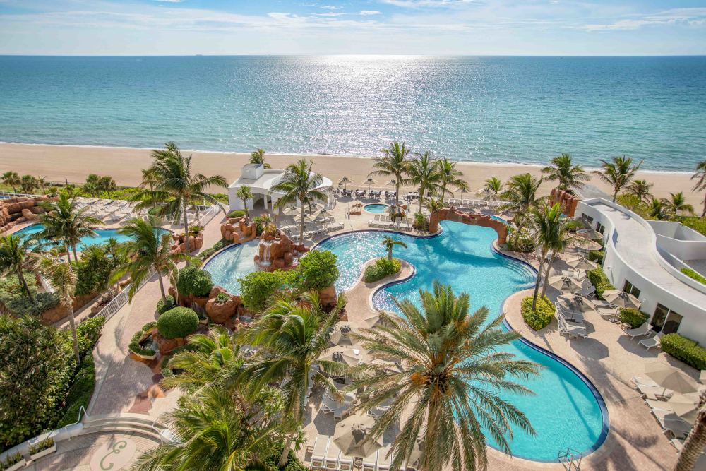 Overview of the pools and crystal blue ocean of the Sunny Isles Beach at Trump International Beach Resort.