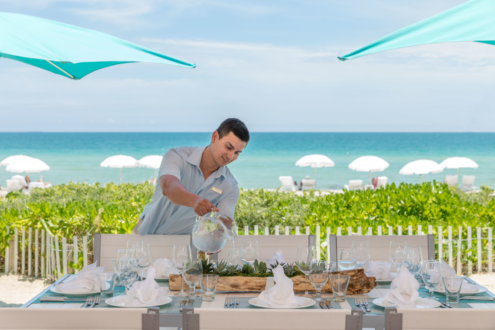 Team member setting up for dining event. Dine with your toes in the sand, overlooking the wide sugar sand beach at Gili's Beach Club, located at the Trump International Beach Resort